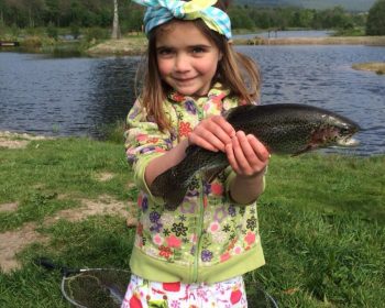 A young girl holding a fish at Rothiemurchus Fishery